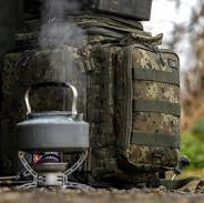Kettle on a camping stove with a camouflage backpack in the background